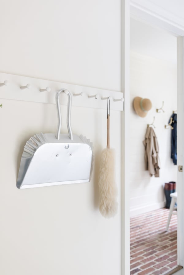 A white mudroom with brick floors and simple mudroom storage bench and hooks.