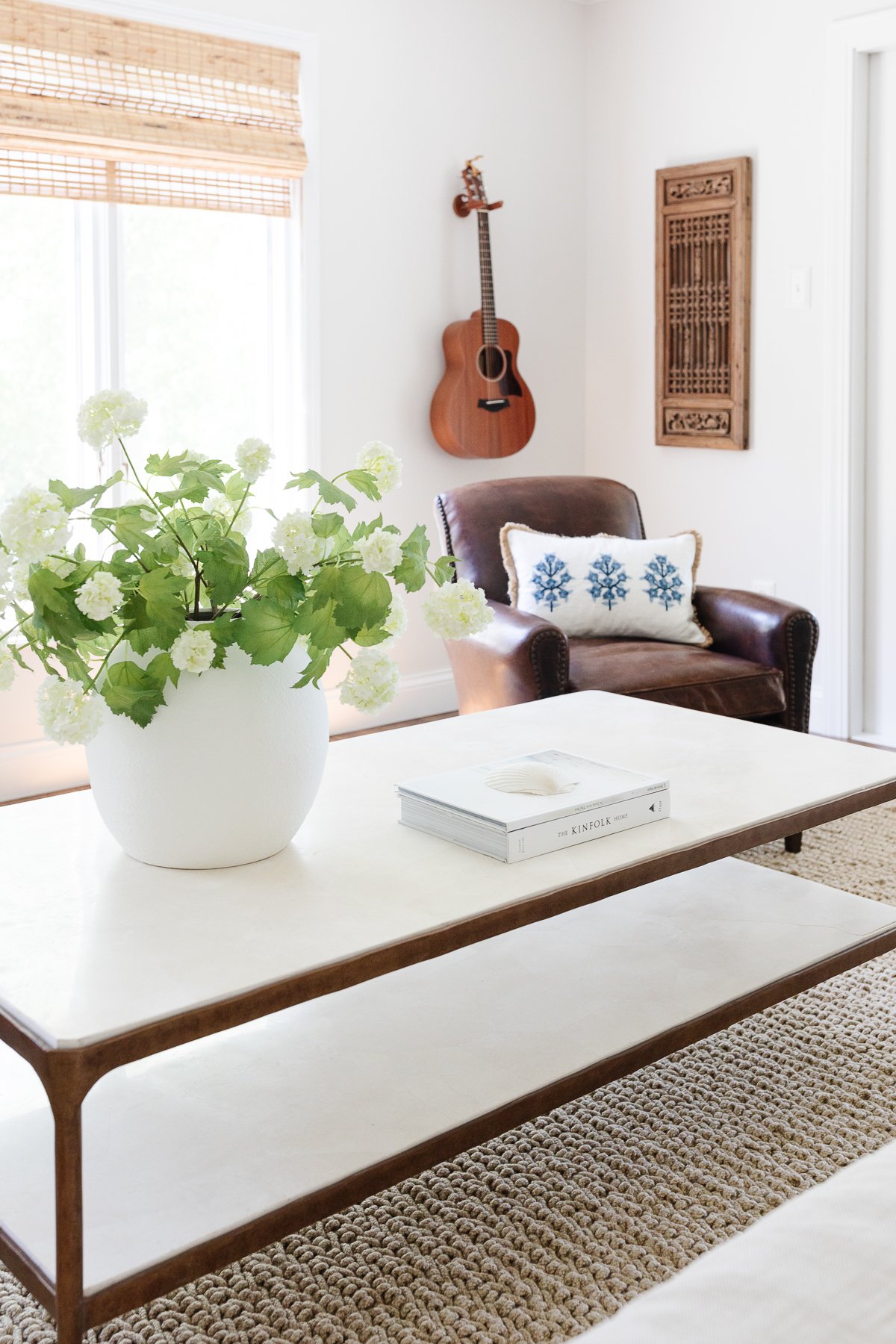 In the music room, there is a vase of flowers on the table and a guitar hanging on the wall in the background.