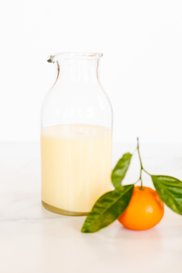 A glass jar of orange glaze, with a small orange in front.