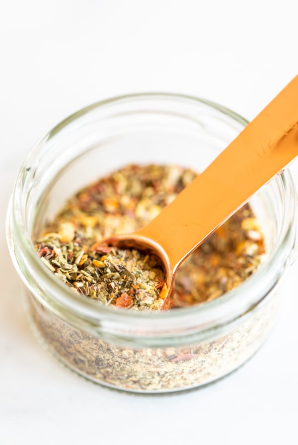 Measuring spoon scooping oregano seasoning from jar