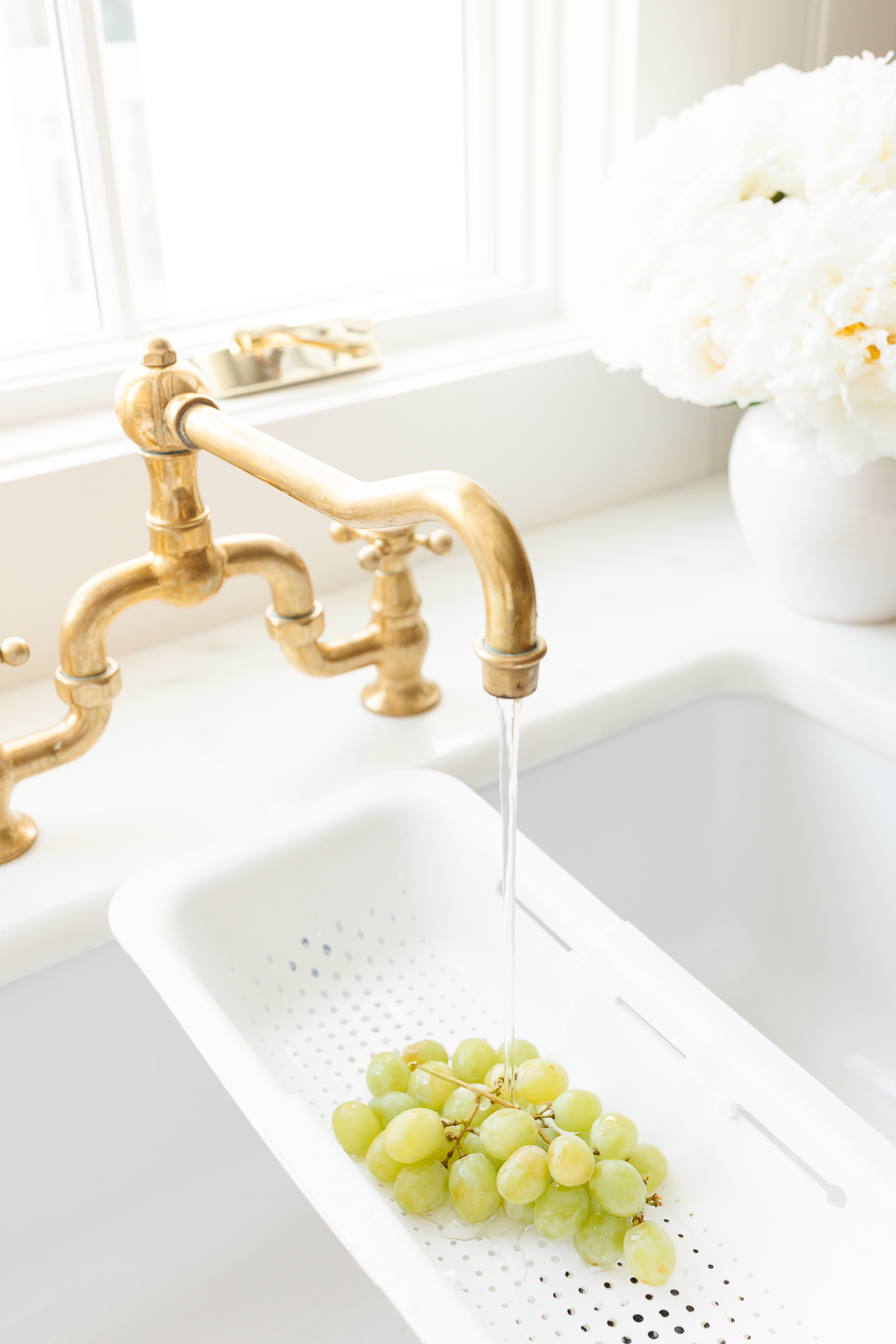 Over-the-sink strainer being used to rinse bunch of green grapes