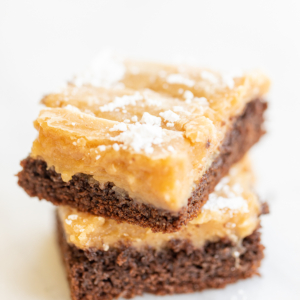 Two slices of ooey gooey butter cake stacked on a white surface.