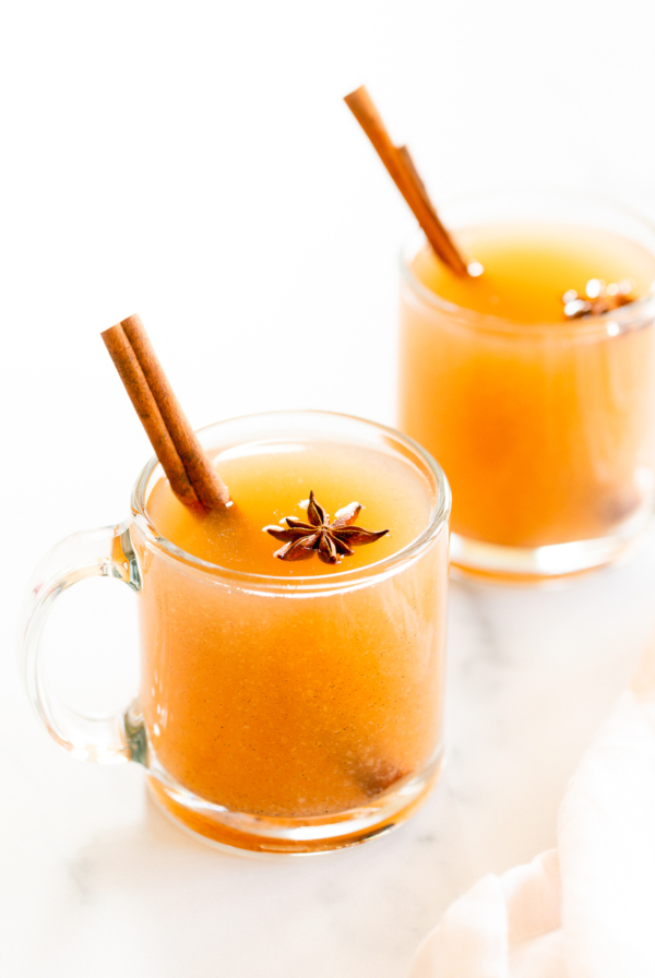 two clear glass mugs of pear cider on a white surface