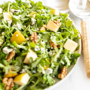 A white bowl full of pear salad, with arugula, walnuts and gorgonzola.