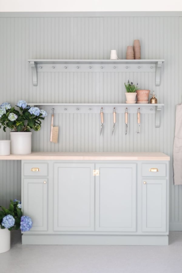 A potting bench painted in a green gray color, flowers and tools on top