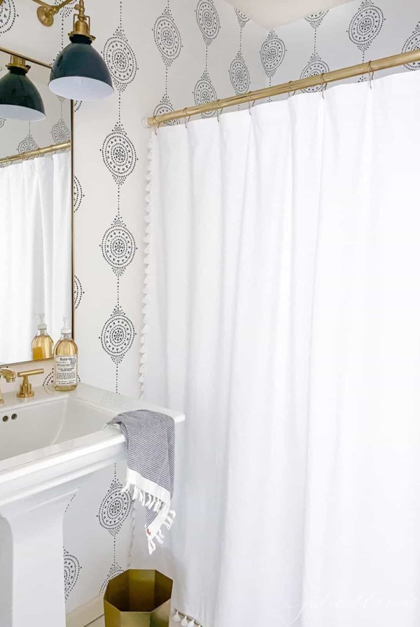 A modern bathroom with a navy light fixture and navy and white patterned bathroom wallpaper.