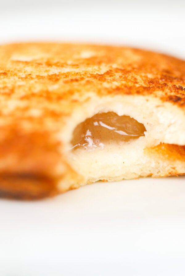 Close-up of a grilled cheese sandwich with melted cheese and a glimpse of brown sauce inside, on a white background.