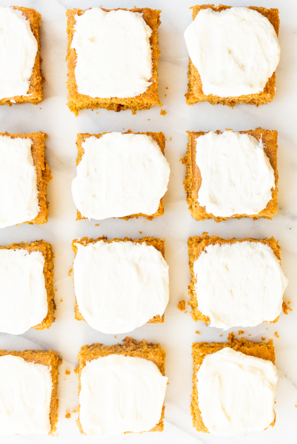 Pumpkin bars with cream cheese frosting on a marble surface.