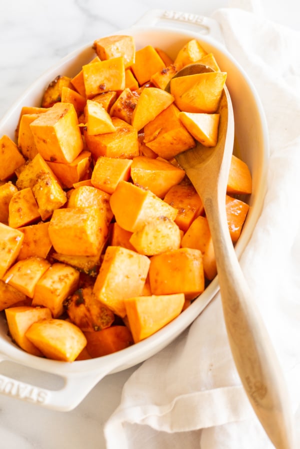 A white oval baking dish filled with roasted sweet potatoes.