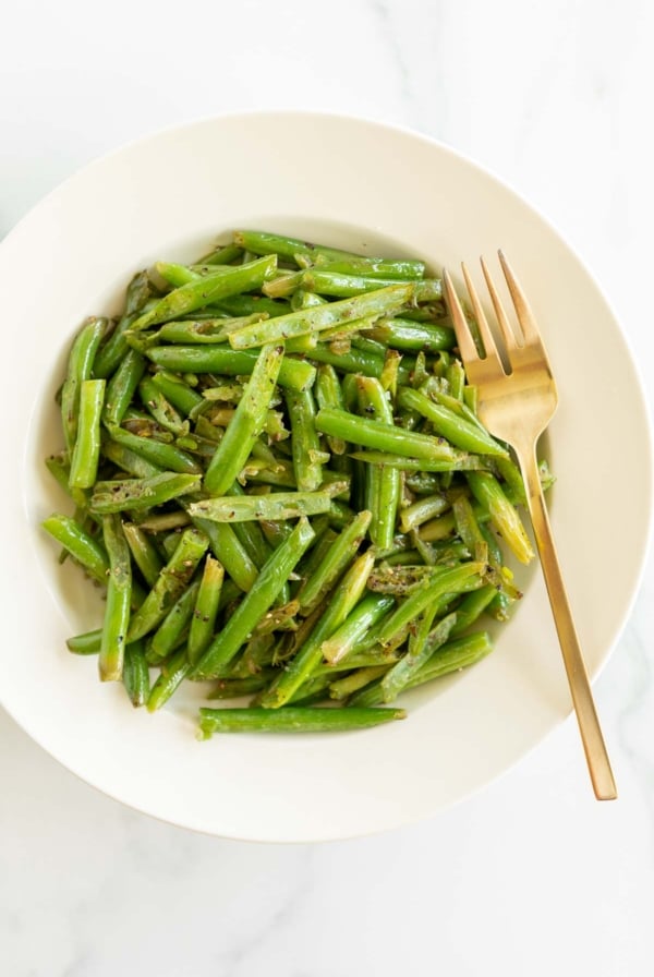 A white plate full of seasoned green beans as a steak side dish