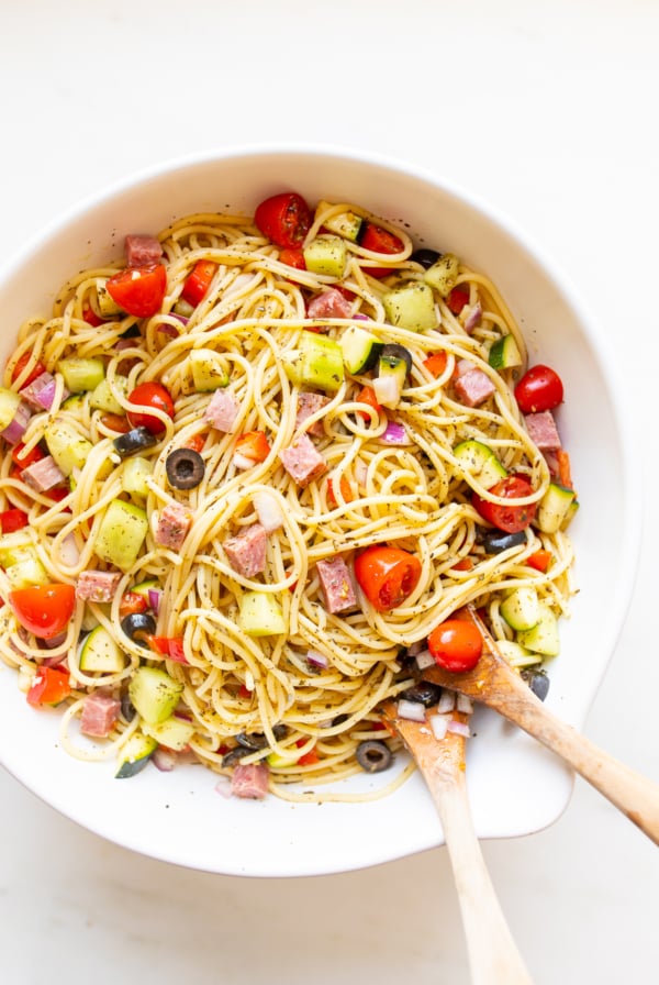 Spaghetti salad in a white bowl with wooden spoons for serving.