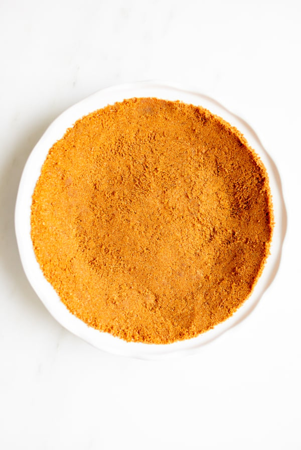 A white pie pan full of speculoos cookie crust for a pie.