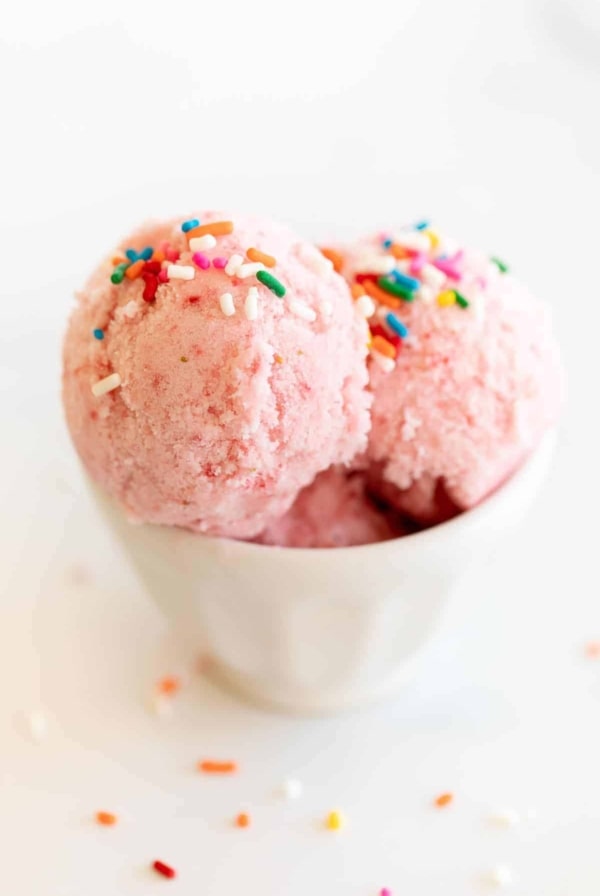 A white bowl of strawberry snow ice cream topped with rainbow sprinkles.