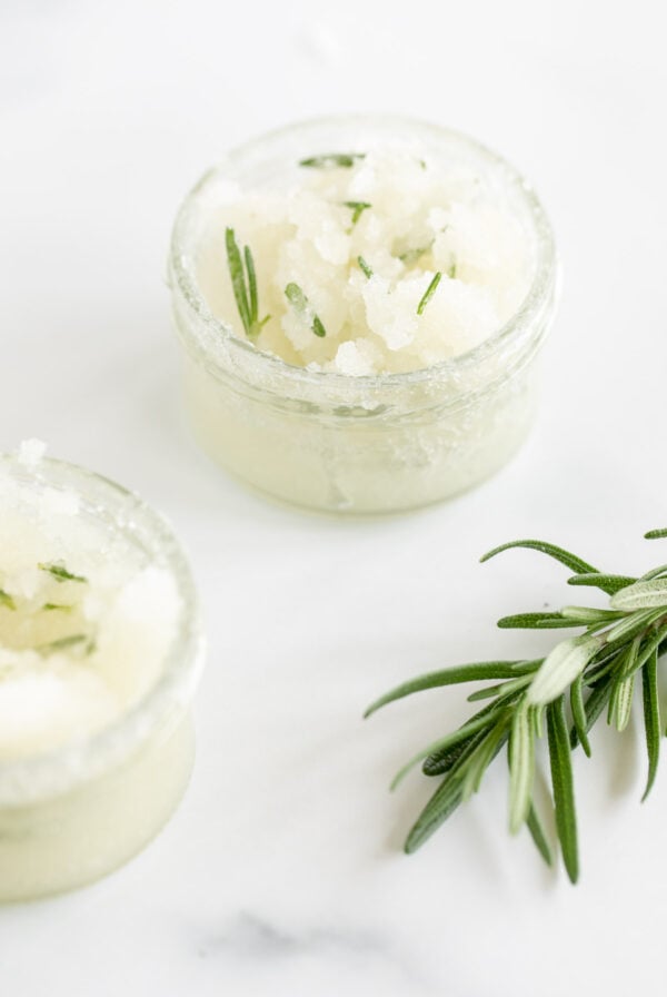 A homemade sugar scrub in a small glass jar with fresh rosemary.