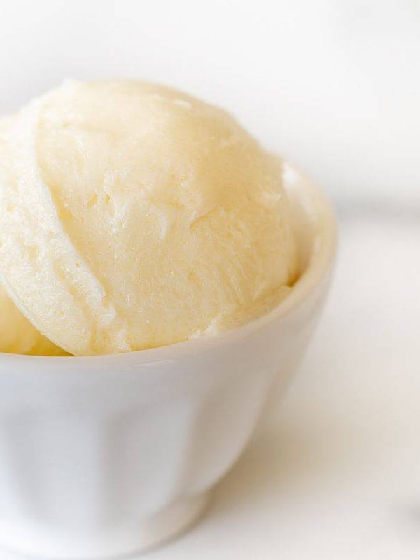 A small white bowl full of sweet butter on a marble counter top.