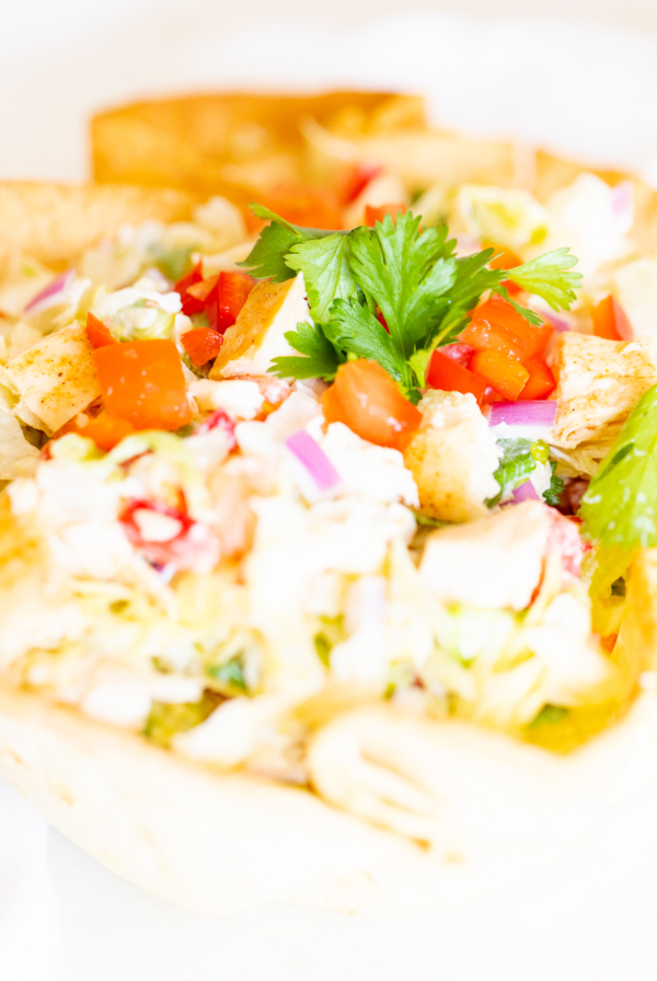 A chicken taco salad in a homemade tortilla bowl on a white plate.