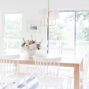 A teak dining table with white chairs and a vase of flowers.