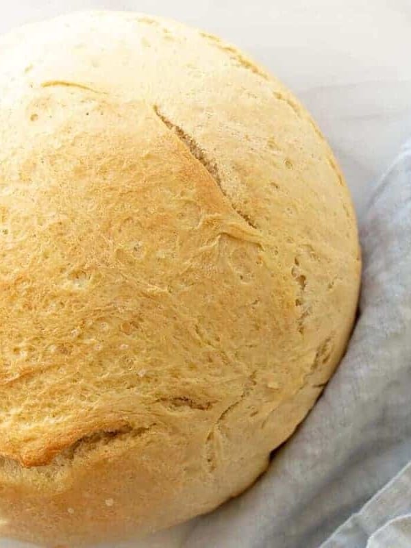 A round loaf of bread made with instant yeast on a marble surface, blue linen napkin to the side.