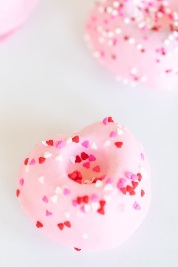 Heart shaped Valentine doughnuts on a white surface, covered in pink icing and sprinkles.