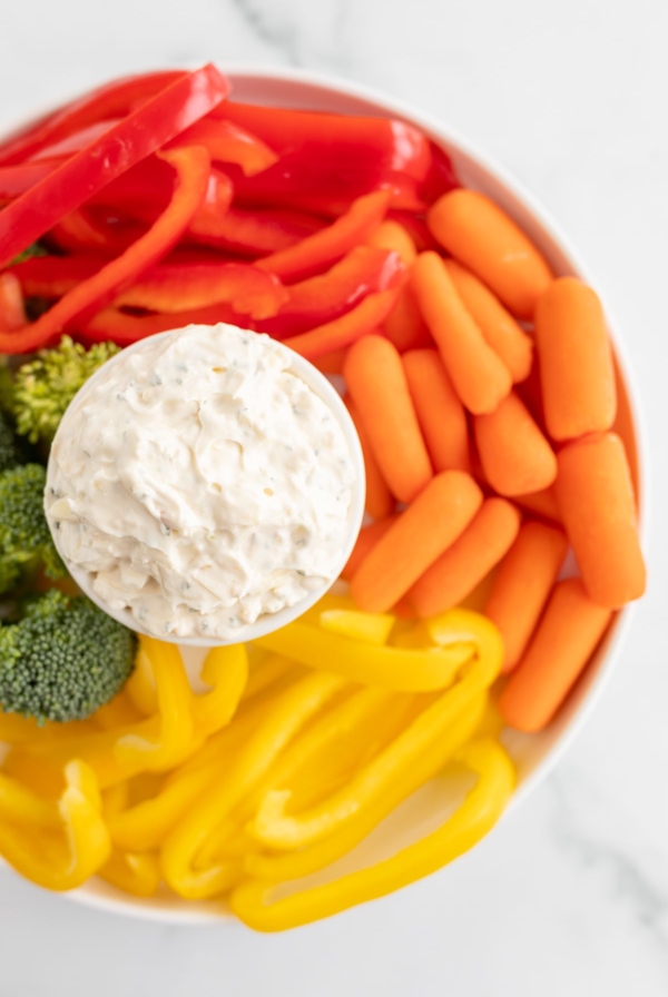 A white bowl full of vegetable dip, surrounded by cut vegetables.