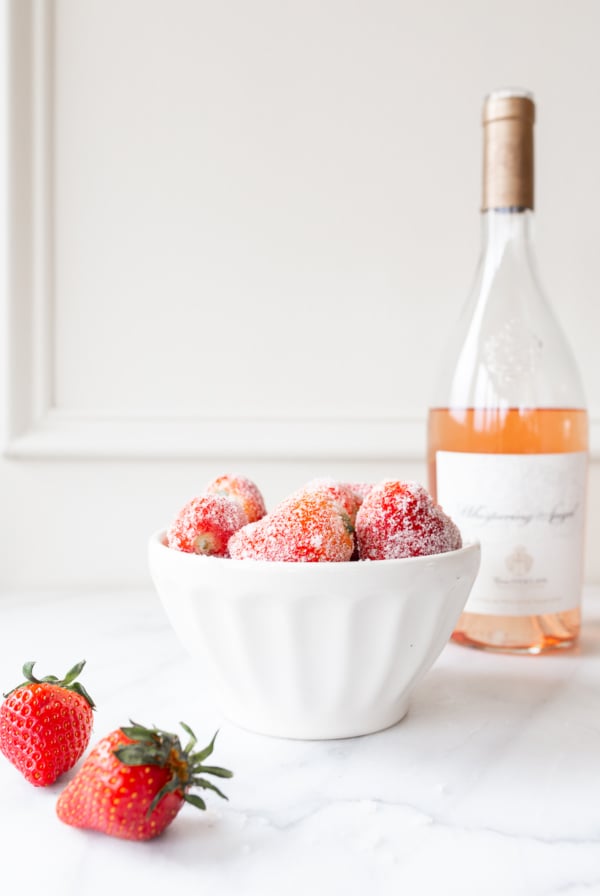 rosé marinated drunken strawberries in a white bowl, bottle of wine in the background.